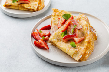 Crepes served with cream cheese and fresh strawberry on white background. 