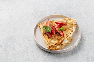 Crepes served with cream cheese and fresh strawberry on white background. 