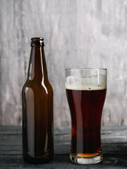 Beer bottle and glass with dark lager on wooden background