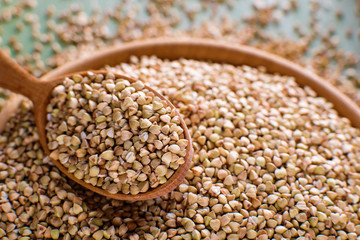 Green buckwheat wooden spoon in a wooden bowl on a wooden table, selective focus