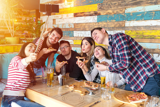 Cheerful young friends taking selfie with smart phone while sharing a pizza 