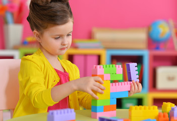 Little girl with stylish hairstyle wearing yellow jacket playing with colorful plastic blocks