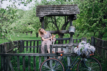 blonde girl in a dress smiles and hugs a dog breed Jack Russell Terrier sitting on a well against the background of a bicycle