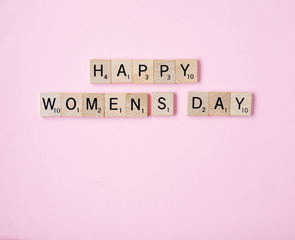 Top view Message happy woomans day spelled in wooden blocks on pink background. Love, 8 march...