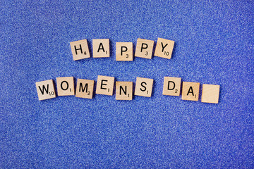 Top view Message happy woomans day spelled in wooden blocks on blue background. Love, 8 march background. Gift, greeting, compliment concept. Copy space. place for text