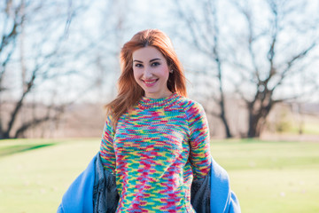  Nice smiling redhead woman with good mood at spring day, casual style, girl wearing wool rainbow sweater 