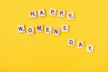 Top view Message happy woomans day spelled in wooden blocks on yellow background. Love, 8 march...