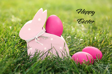 Easter eggs with wooden bunny toy on green grass outdoors