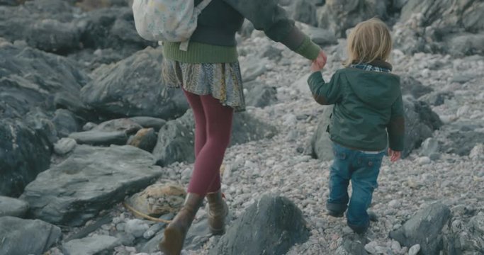 Mother and toddler walking hand in hand on beach in winter