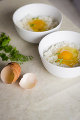 Two cups with fresh egg yolk is on the top of Japanese rice.