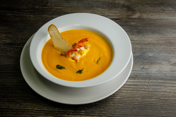 yellow fish cream soup decorated with prawns tails and one slice of dried bread