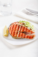 Grilled red salmon steak served with lemon and lettuce on white plate. Sockeye salmon, kokanee salmon or Oncorhynchus nerka.
