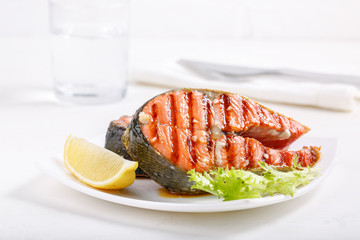 Grilled red salmon steak served with lemon and lettuce on white plate. Sockeye salmon, kokanee salmon or Oncorhynchus nerka.
