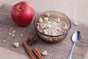 Healthy food. Muesli in a bowl on a light background with a red delicious apple. Breakfast porridge on linen background