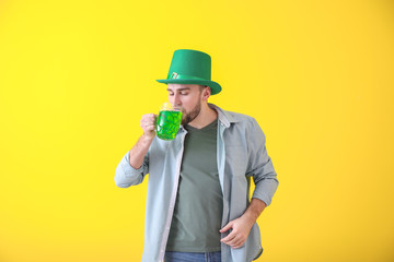 Handsome young man in green hat drinking beer on color background. St. Patrick's Day celebration