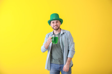 Handsome young man in green hat and with mug of beer on color background. St. Patrick's Day celebration