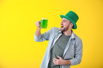 Handsome young man in green hat and with mug of beer on color background. St. Patrick's Day celebration