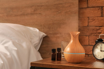 Aroma oil diffuser with bottles on table in bedroom