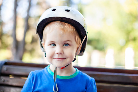 Little blonde boy 3 years old in white sport helmet and blue t-shirt outside. Special problems with kid's eyes. Myopie, astigmatism, cross-eyed