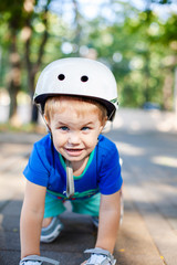 Little blonde boy 3 years old in white sport helmet and blue t-shirt riding on the roller-slates in the summer green park. Special problems with kid's eyes. Myopie, astigmatism, cross-eyed