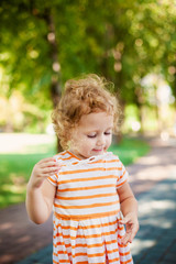 Little blonde curly girl blowing soap bubbles in summer park