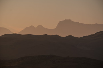 A silhouette of the Langdale Pikes skyline created by evening light, seen from Loughrigg Fell, Lake District, UK