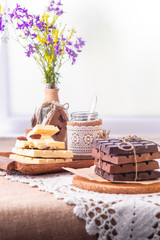 Still life with dark, milky and white chocolate bars, dishes and wild flowers bouquet of against window