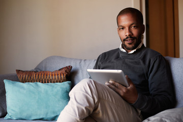 Handsome African black man using tablet on sofa couch in home living room
