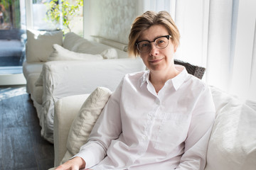 Portrait of a happy middle aged woman with glasses sitting on a sofa