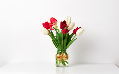 tulip flowers are in a vase on the table, white wall as background