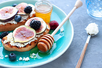 Bruschettas with fresh ripe summer berries, figs and cheese on the plate. Breakfast close up.