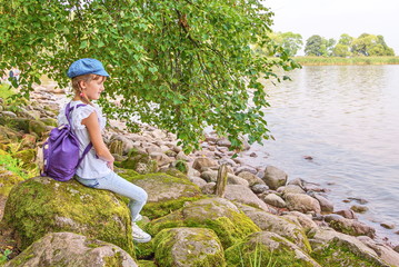 Little girl sits on large stones on  shores of  Gulf of Finland Baltic Sea