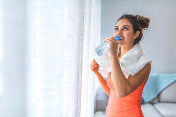 Fit young woman drinking water at the home. Muscular woman taking break after exercise.