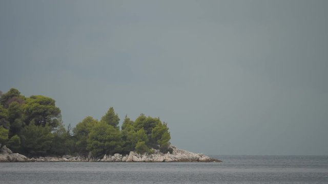 Rocky coast with pine trees and sea under dark cloudy sky before summer storm