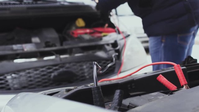 A man using the wires starts the car from the donor with a discharged battery in the winter