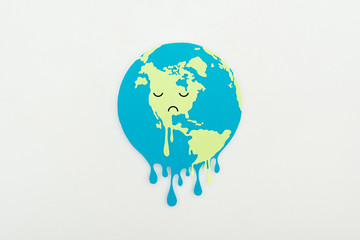 melting paper cut globe with sad face expression on grey background, global warming concept