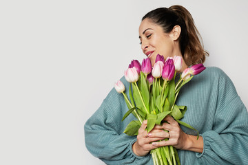 Smiling young girl holding colored tulips bouquet isolated over gray background.