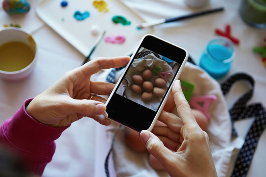 Happy easter decoration. Woman hands holding smartphone and making photo of colorful easter eggs on the table