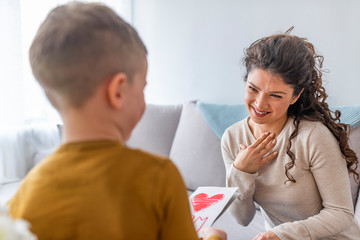 Attractive young woman with little cute boy are spending time together at home while sitting on bed. Happy family concept. Mother's day.