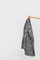 Woman's hand holds a zebra patterned coat. Abstract conception, studio shot on white background.