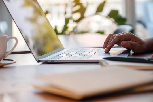 Closeup image of a woman's hand using and touching on laptop touchpad with notebooks and papers on the table in office