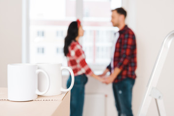 selective focus of cups standing on box with couple holding hands on background