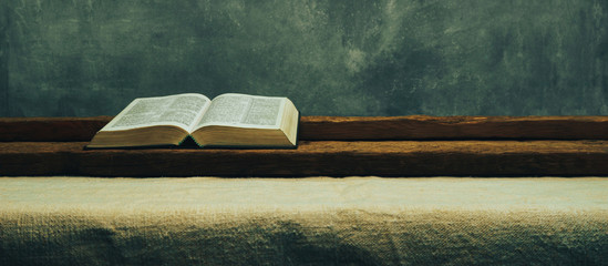 Open Bible on a old table. Beautiful gray wall background. Religion concept.