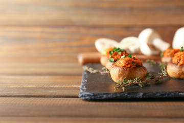 Slate plate with tasty stuffed mushrooms on wooden table