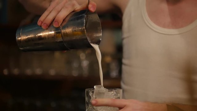 Young professional bartender pouring white crem drink into the glass full of ice 