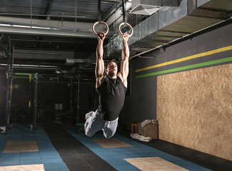 Young sporty man training with gymnastics rings in gym