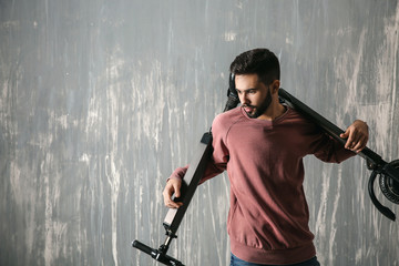 Fashionable young man with kick scooter near grey wall