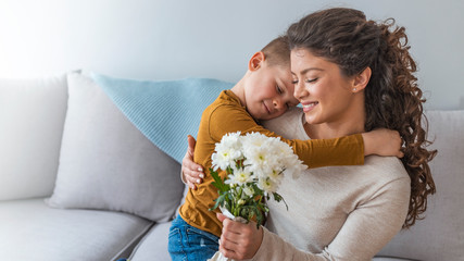 Son hugging happy mother with flowers. Mother`s day concept. Family holiday.