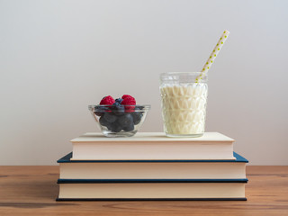 Frische Früchte und ein Glas Milch auf einem Bücherstapel, weißer Hintergrund
