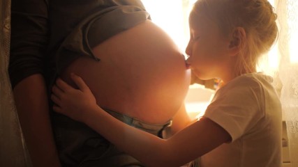 Happy 6 year old daughter kissing mom's pregnant belly. Slow motion, 4K UHD.